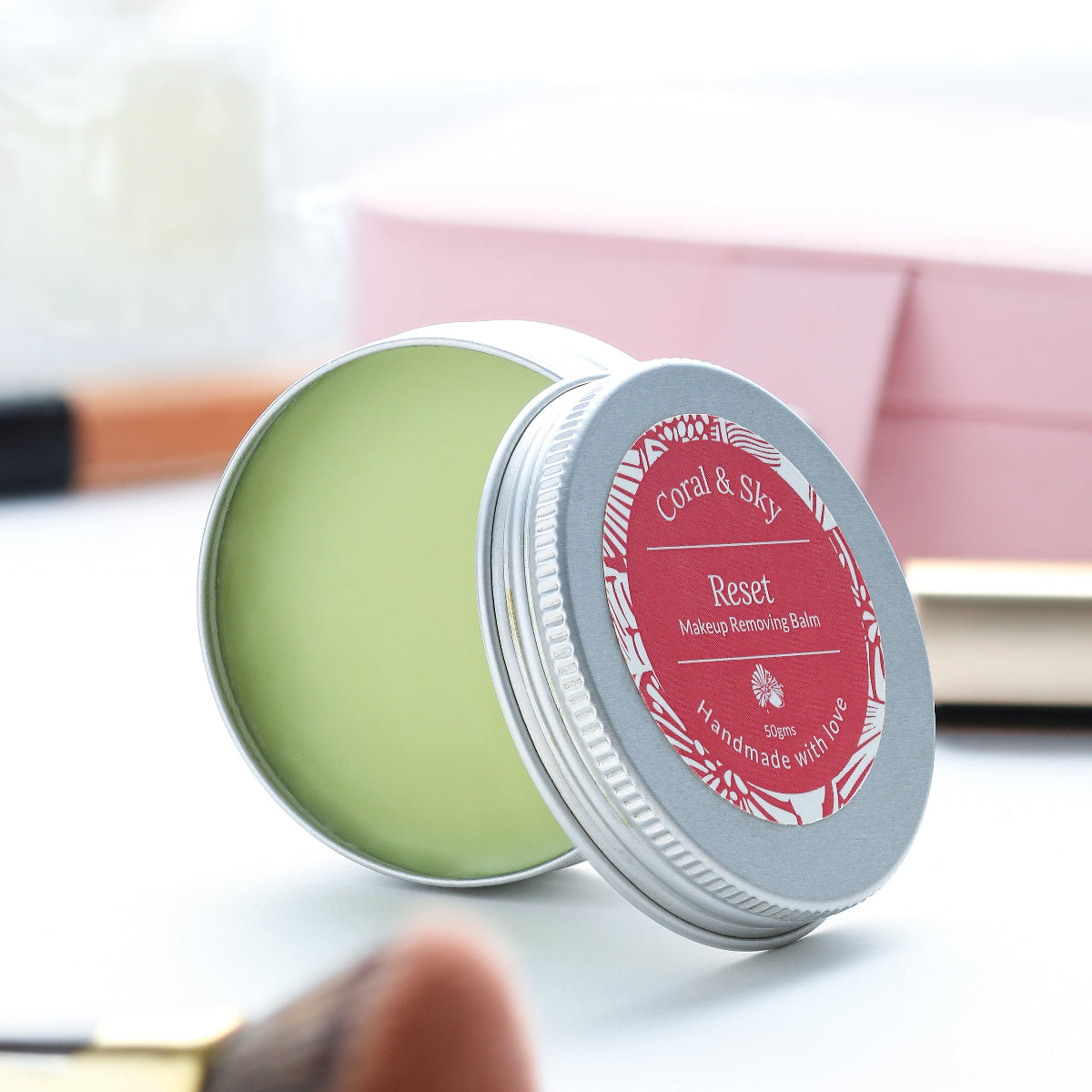 Makeup removing balm in a metal tin with a pink label on a blurred background